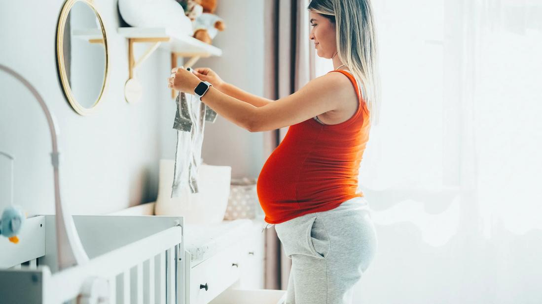 Pregnant person happily folding baby clothes in the nursery