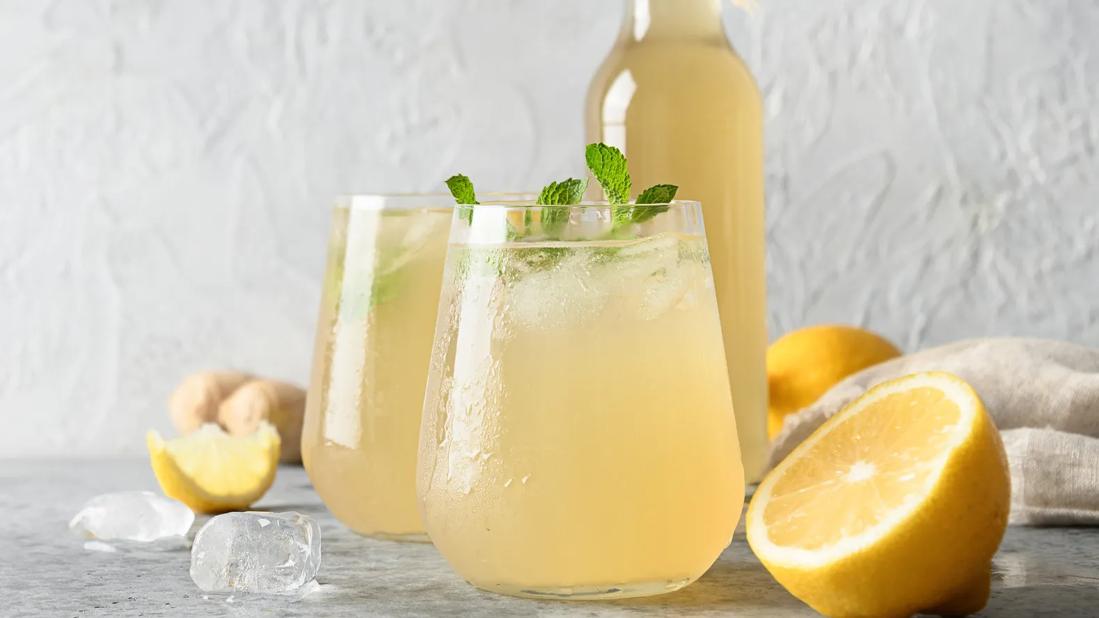 Glasses and bottle of yellow-colored prebiotic soda, with mint, lemon and ginger garnish