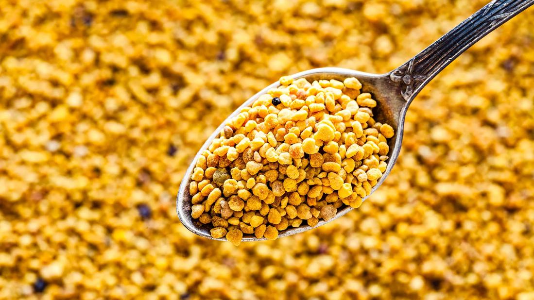 Spoonful of bee pollen granules held up over bee pollen granules