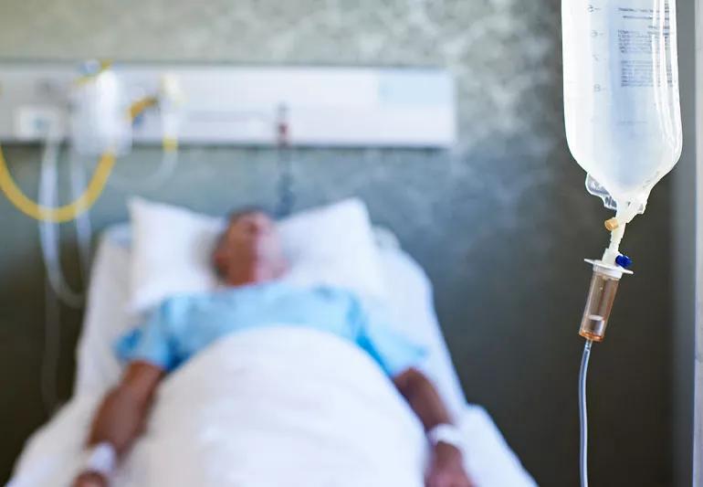 Man in coma in hospital with IV hanging in foreground.