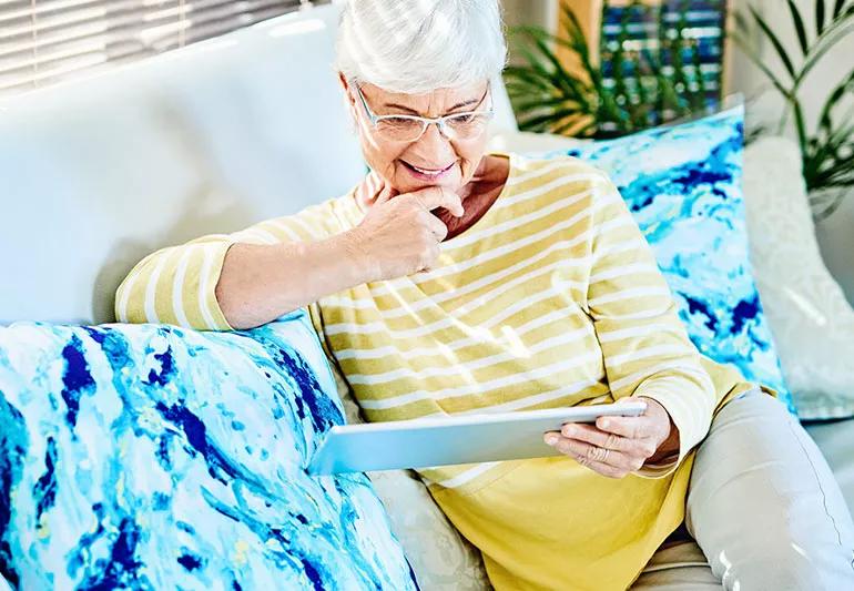 Elderly person reading on tablet computer in the Living room of their home.