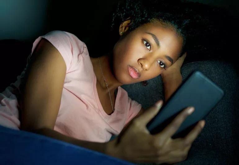 sad teen girl accesses her smart phone at night