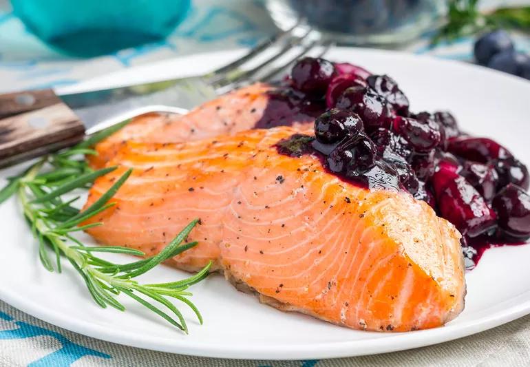 Closeup of cooked salmon plated with a garnish of chunky blueberry sauce.