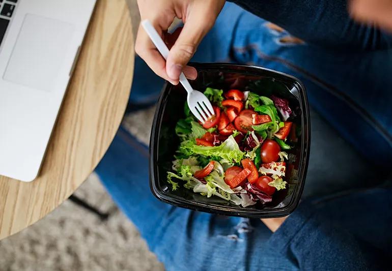 Closeup of person using a white fork in a to-go container of salad