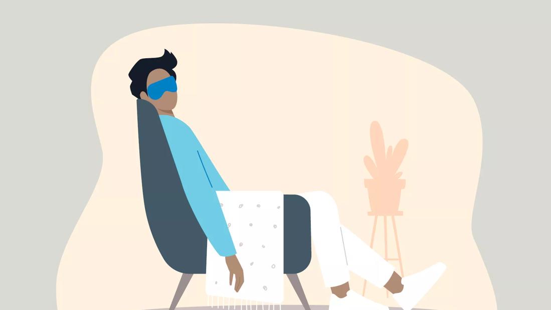 Person asleep in a chair with an eyemask on and a blanket over their lap