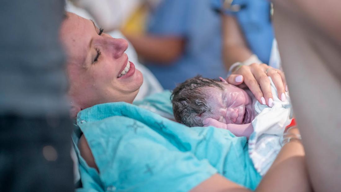 Smiling mother holding just-born baby in hospital