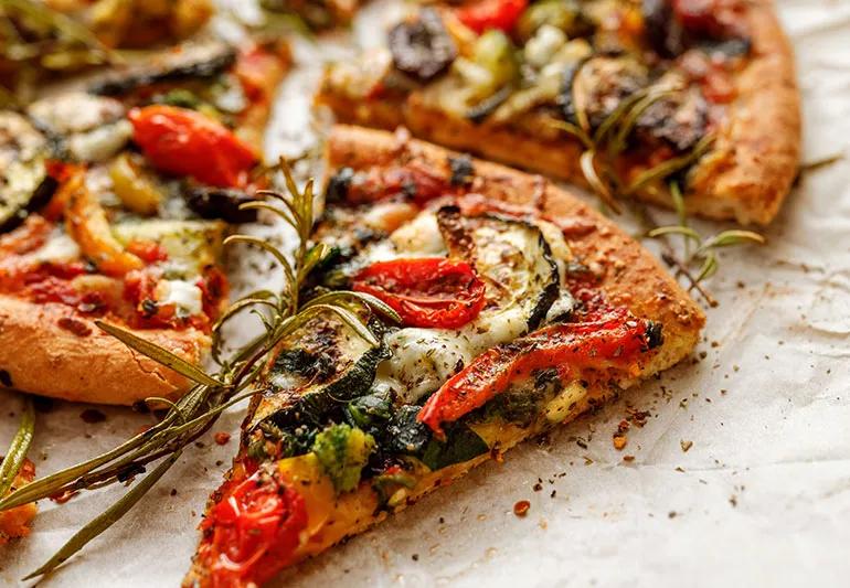 A close up of a meatless pizza with tomato, cheese, broccoli and herbs