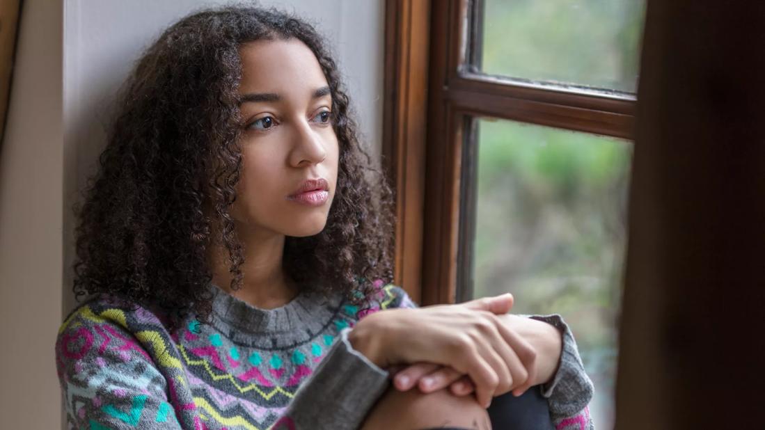 Teen sitting in window well staring out the window