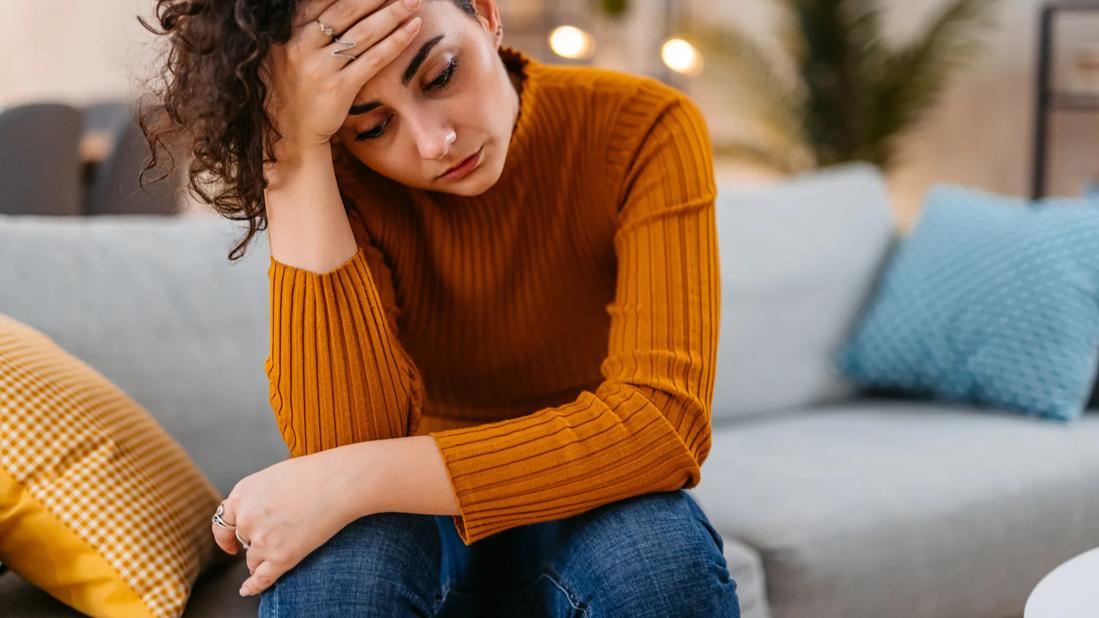 Person sitting on couch with head in hand, looking upset/stressed