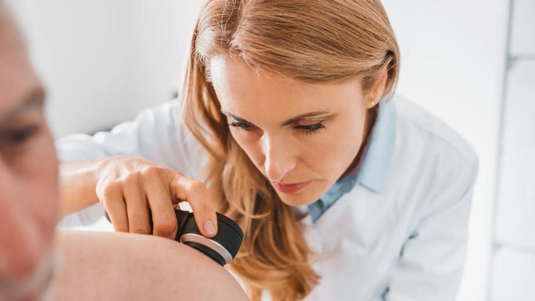 Dermatologist using magnifying tool to look at spot on person's back