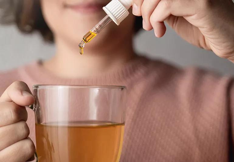 A person drops CBD oil into a clear glass of liquid.