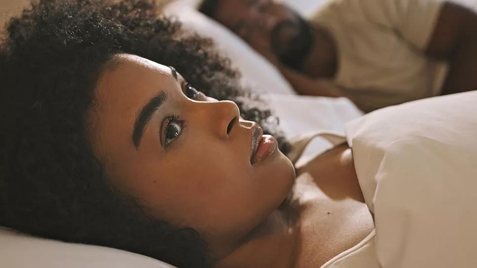 female awake in bed staring ahead with male next to her asleep