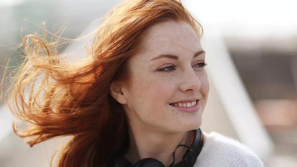 Female with red hair, freckles and light-colored eyes outside in the sun