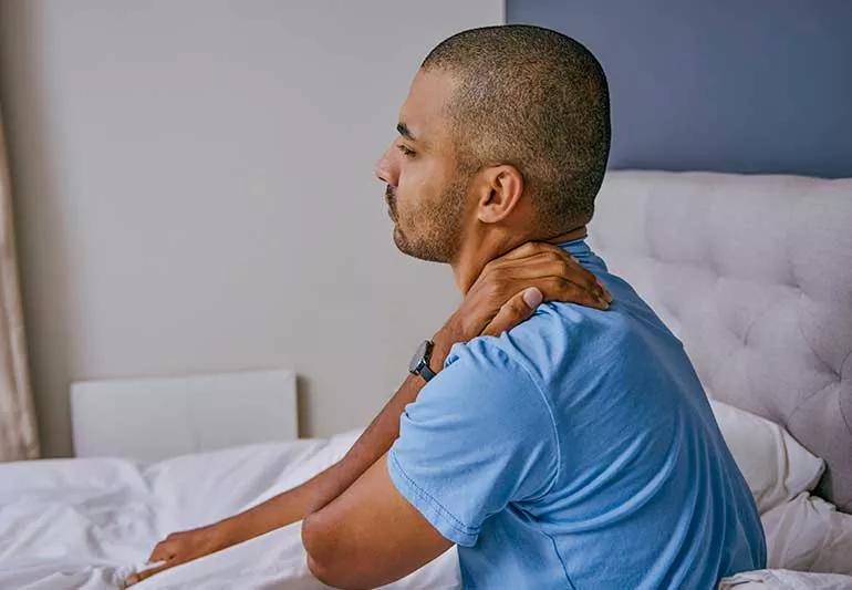 person sitting up in bed and rubbing neck