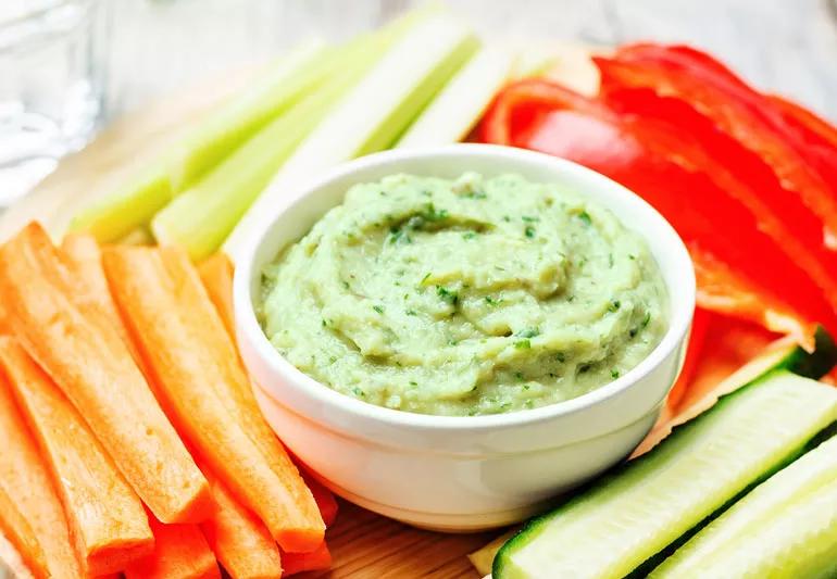 Garden chive bean dip in bowl on tray with cut vegetables.