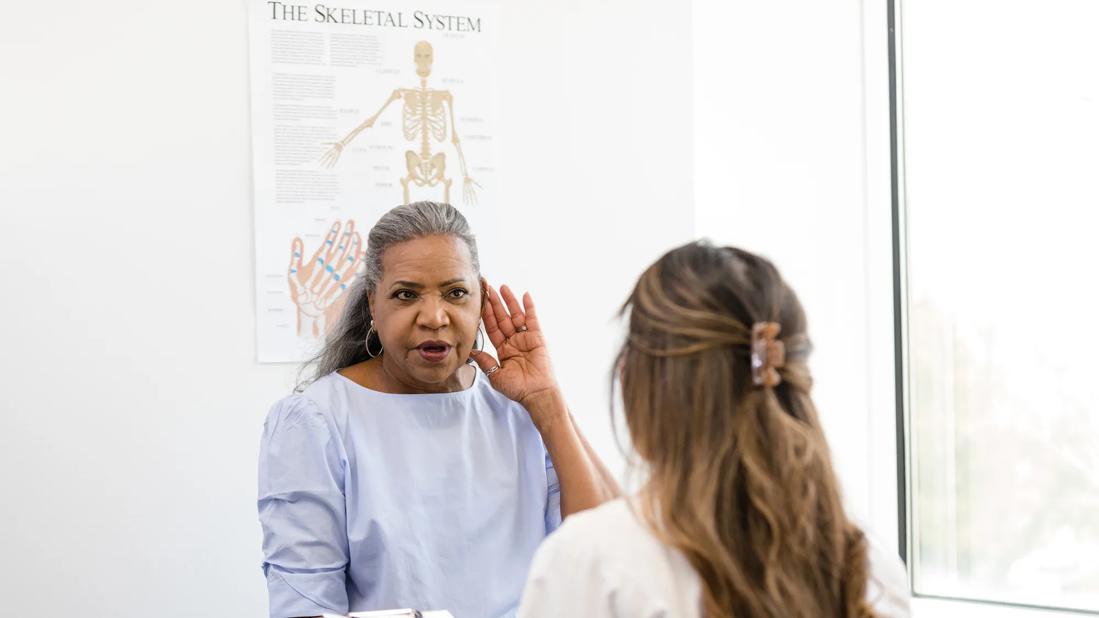 Woman cupping her hand to her ear trying to hear the healthcare provider