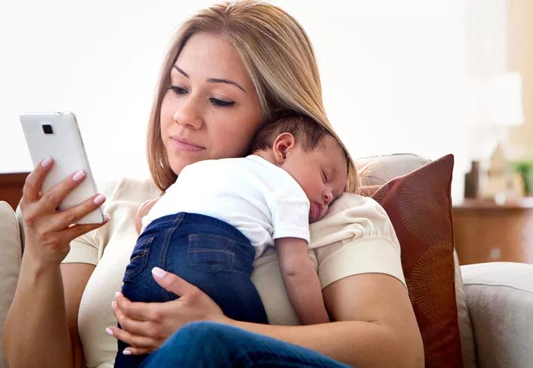 Mom holding newborn and checking smartphone