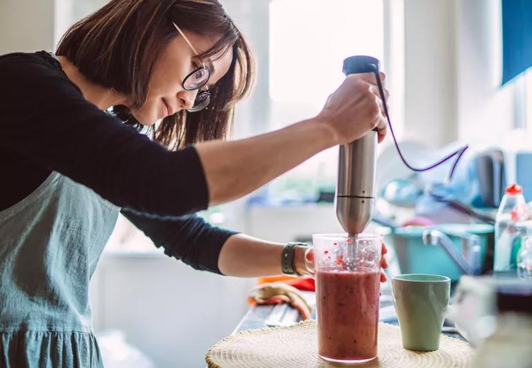 A person using a handheld blender to make a smoothie