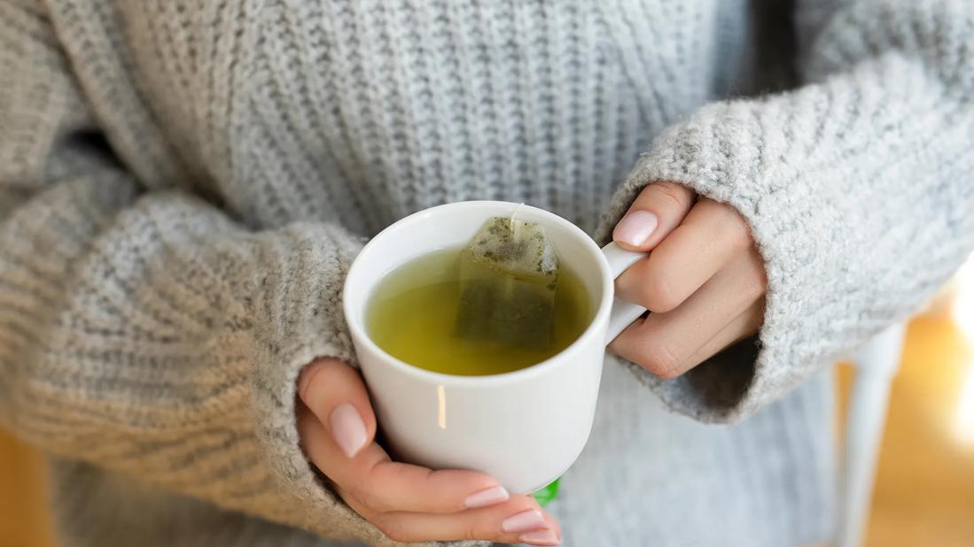 Person in bulky sweater, with their hands holding cup of tea with tea bag in it