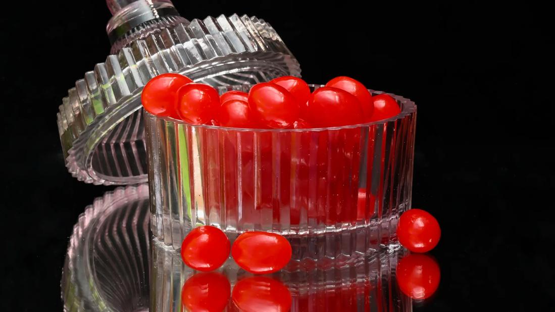 Bright red jelly beans in crystal container with lid on black background