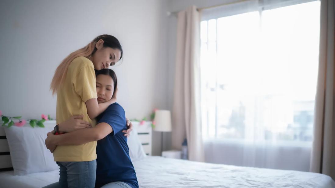 Person sitting on bed hugging person standing