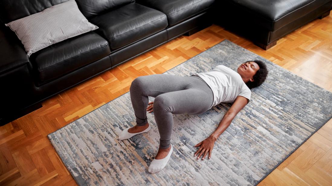 Person doing yoga bridge pose in living room by sofa