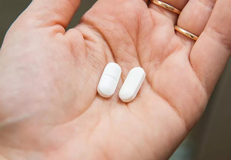 A close up image of a person holding two, oval-shaped white pills