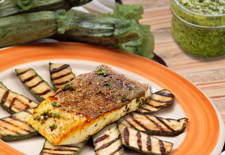 Halibut on slices of grilled zucchini with pesto in background