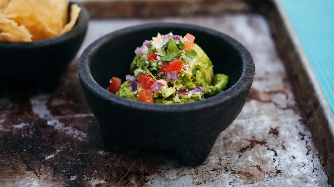 Motar of mediterranean guacamole, with motar of corn chips nearby