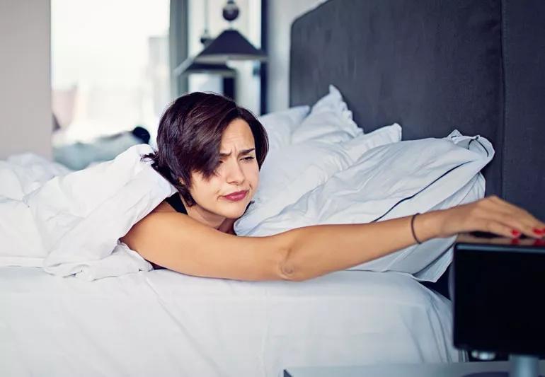 Tired woman turning off bedside alarm clock