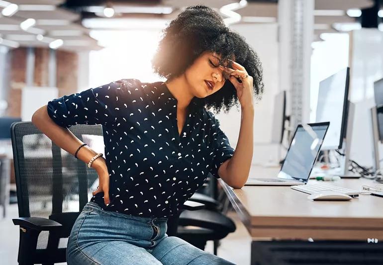 Woman experiencing back pain while working on her computer