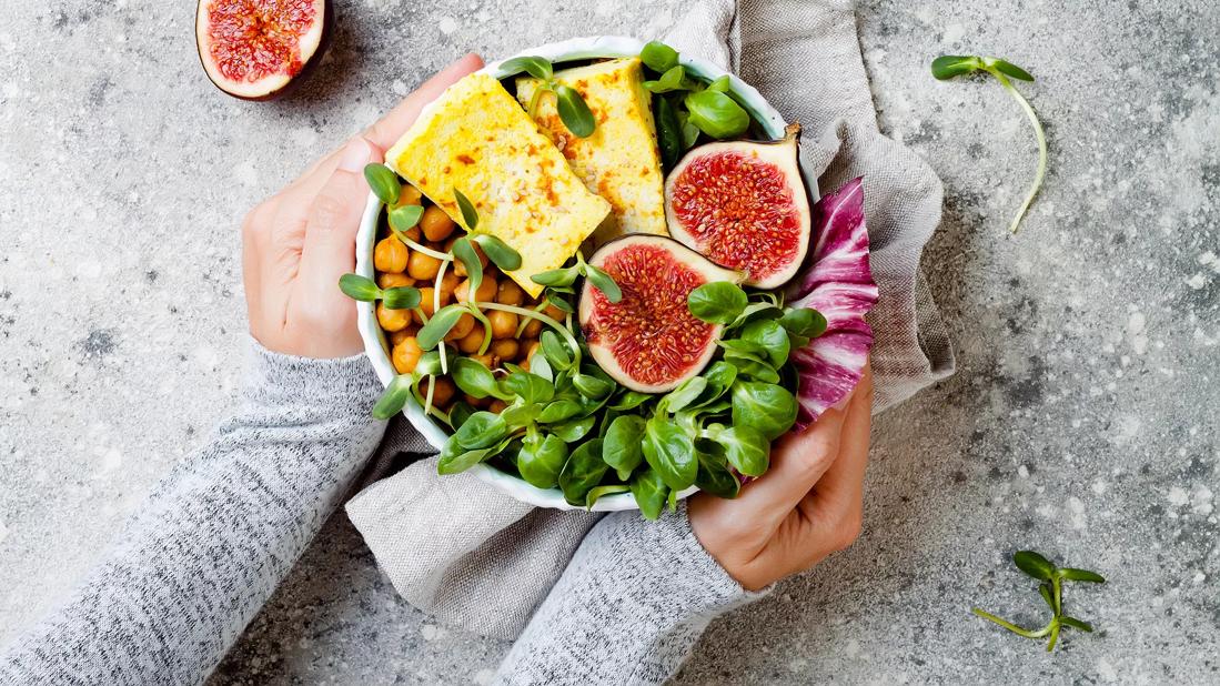 Hands cupping bowl of greens, chickpeas, whole figs, halved and tofu