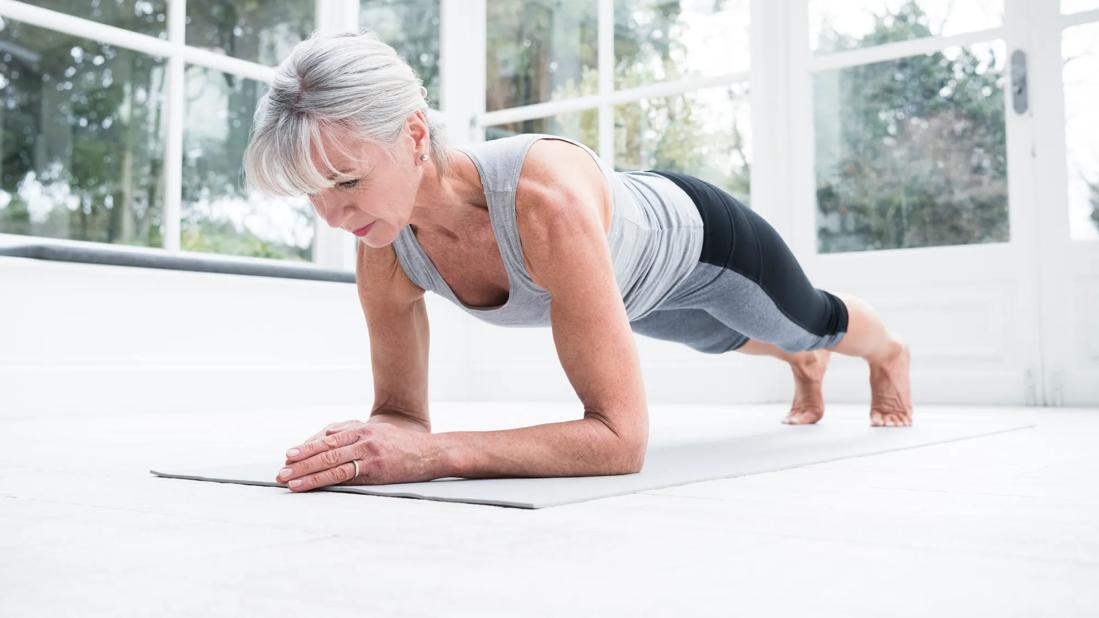 Older person doing a plank on yoga mat in windowed room