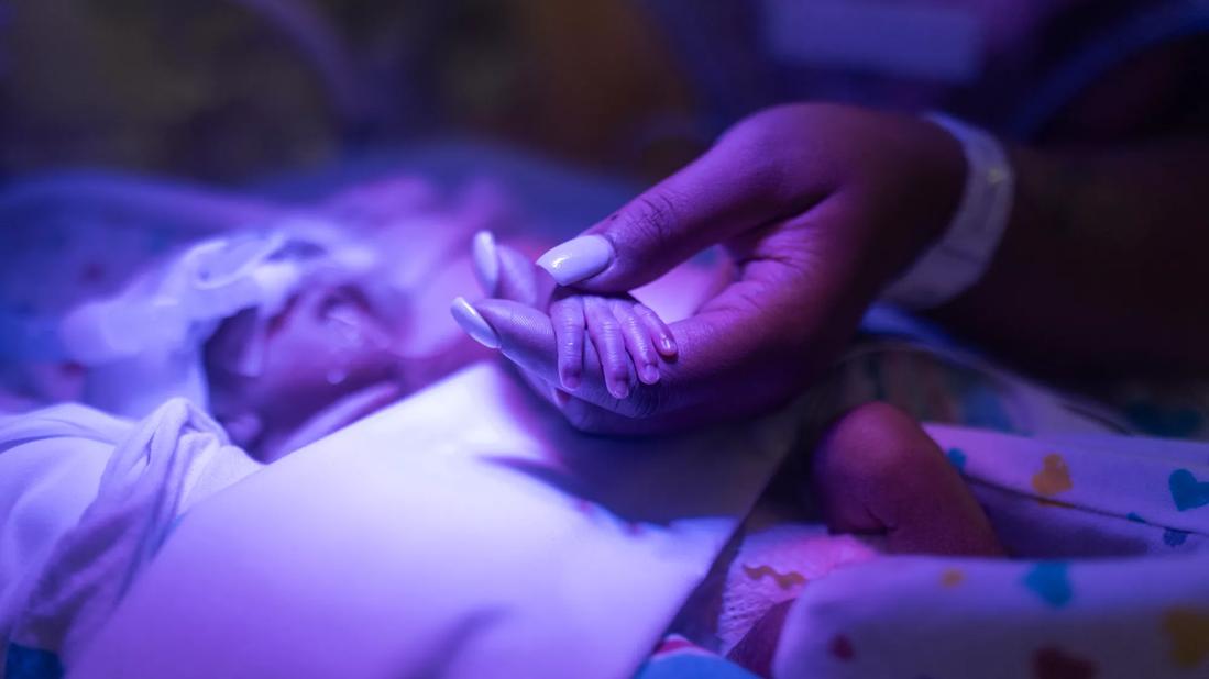 Caregiver holds baby's hand in NICU setting