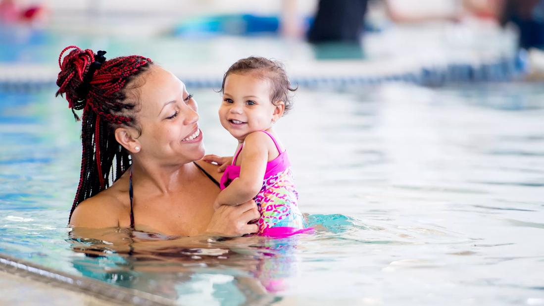 Smiling parent holding smiling baby in a pool