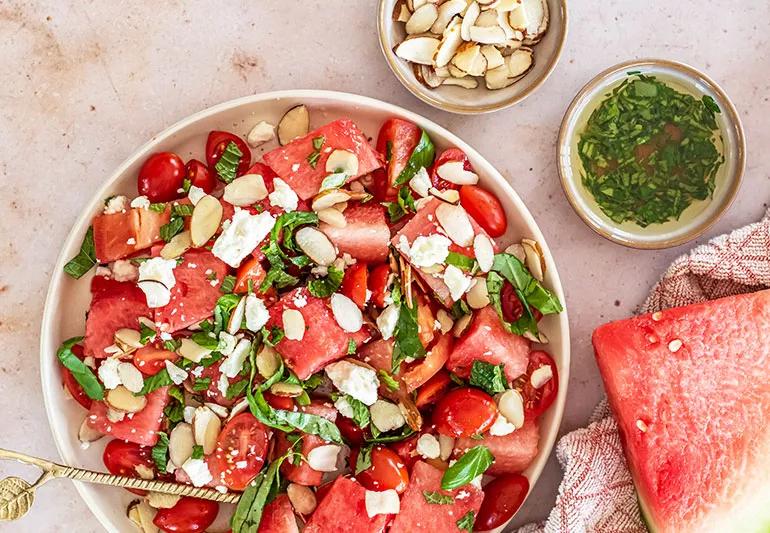 A bowl of watermelon salad with feta cheese, herbs and sliced almonds