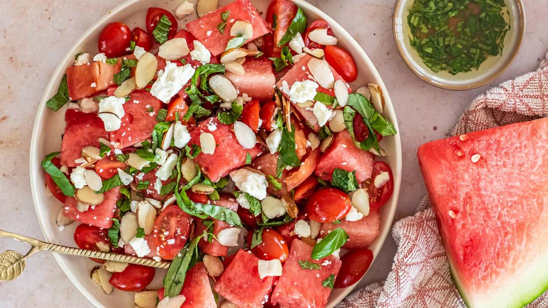 A bowl of watermelon salad with feta cheese, herbs and sliced almonds