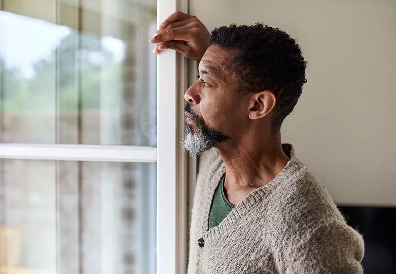 Person looking wistfully out a window with one hand raised above head resting on sill