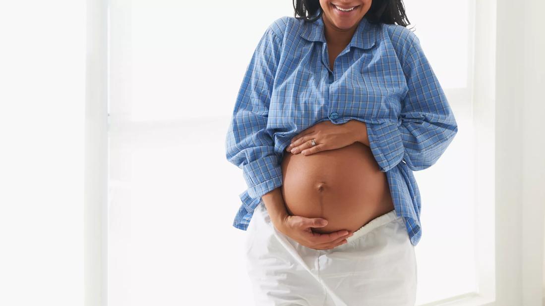 Happy pregnant woman with hands around her belly, with belly button pushing out