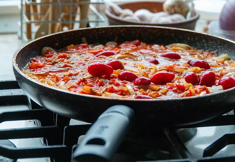 A pan of spaghetti and a sauce full of red cherry tomatoes cooking on a stove