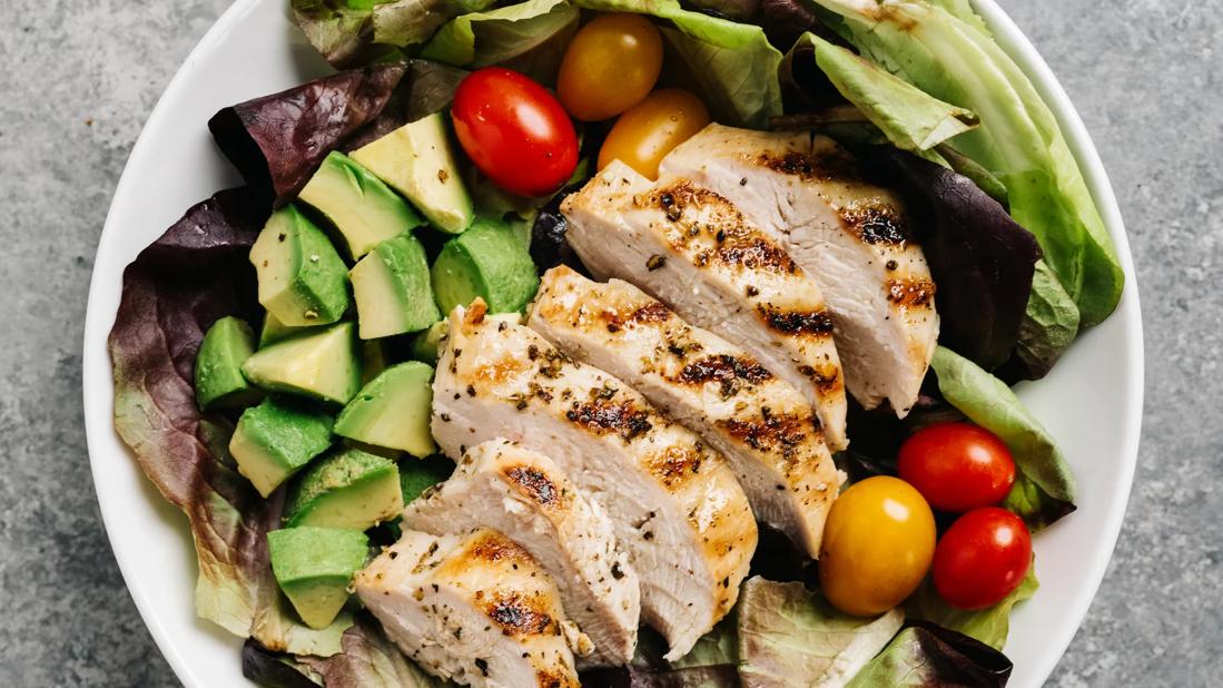 Sliced grilled chicken on greens, with avocado and tomatoes