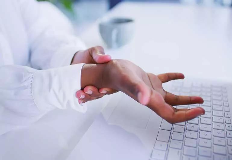 Person holding wrist at computer desk.