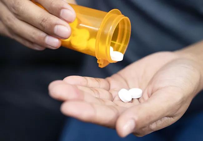 Woman hand with pills on, spilling pills out of bottle on dark background.