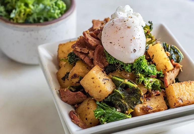 A bowl of hash topped with bacon and a poached egg