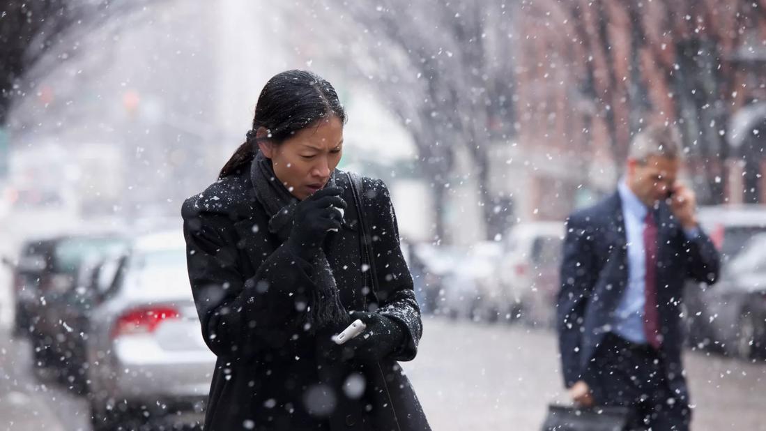 Woman outside in coat during snowy weather covering her mouth