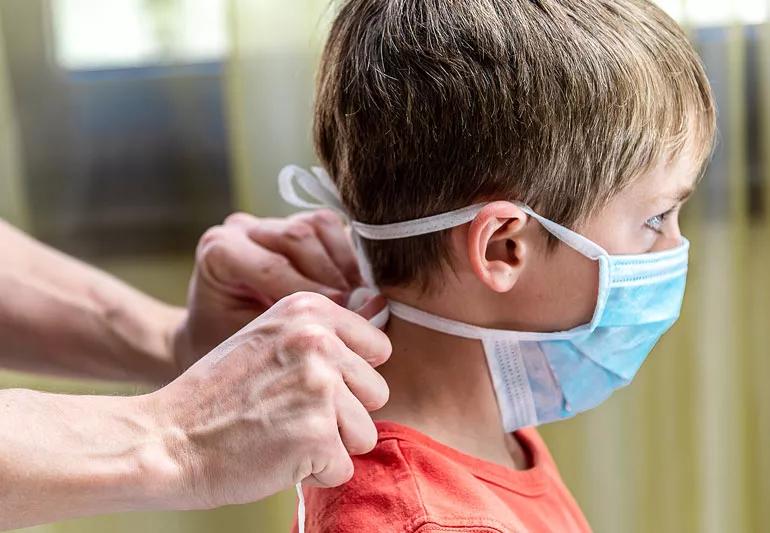 mom tying covid mask on her child for protection