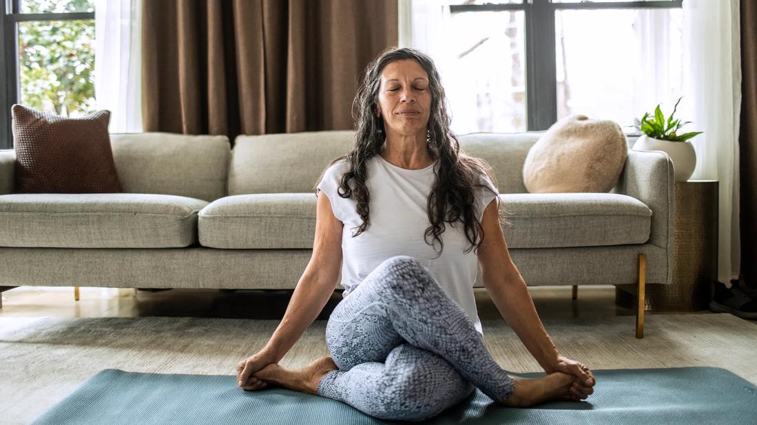 Smiling, relaxing person in a yoga pose on an exercise mat in living room