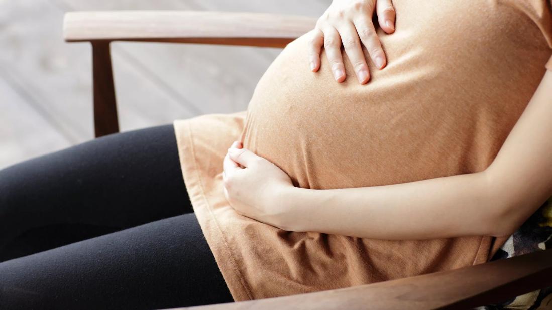 Closeup of person's seated torso with hands holding a pregnant belly