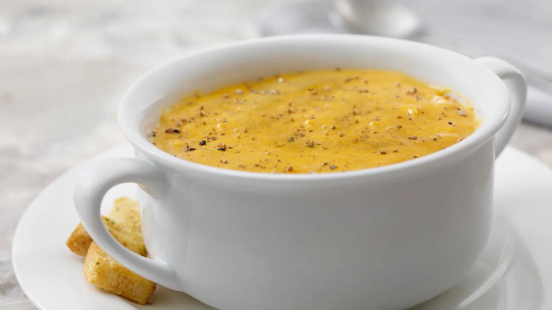 White crock of butternut, carrot and ginger soup on plate