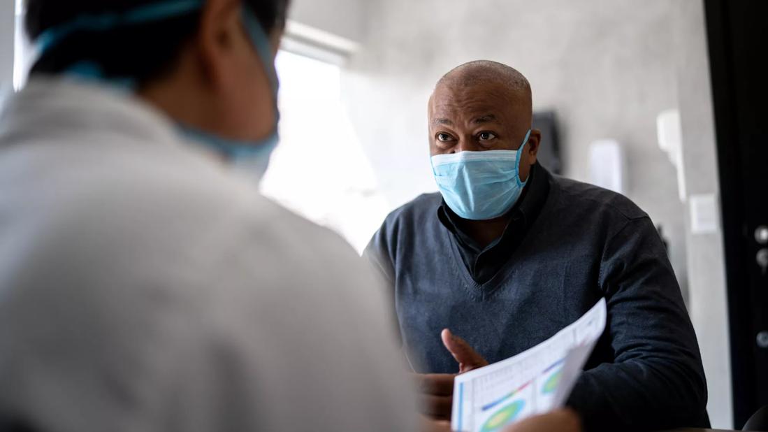 Doctor talking to a patient on medical appointment &#8211; using protective face mask